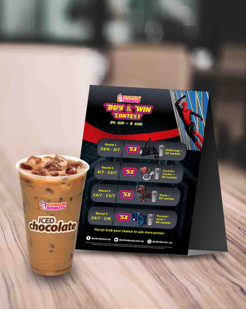 Dunkin’ Donut cup filled with Iced Chocolate drink put in front of table top Dunkin’ Donuts promotional advertisement
