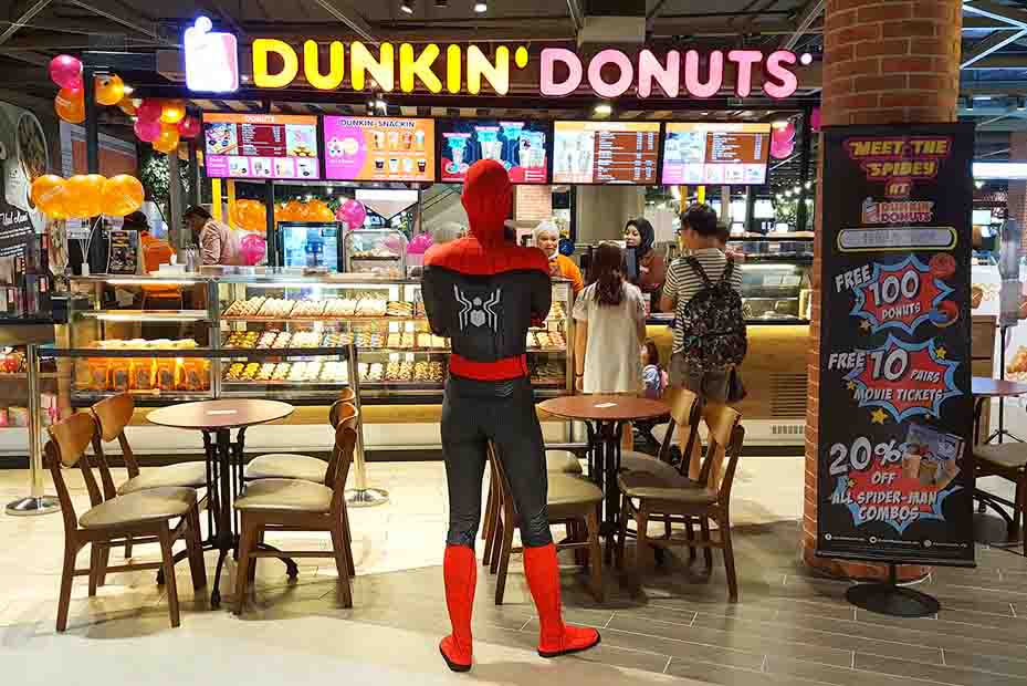 Man in a Spiderman costume facing a Dunkin’ Donuts outlet with his arms crossed and back facing the camera.
