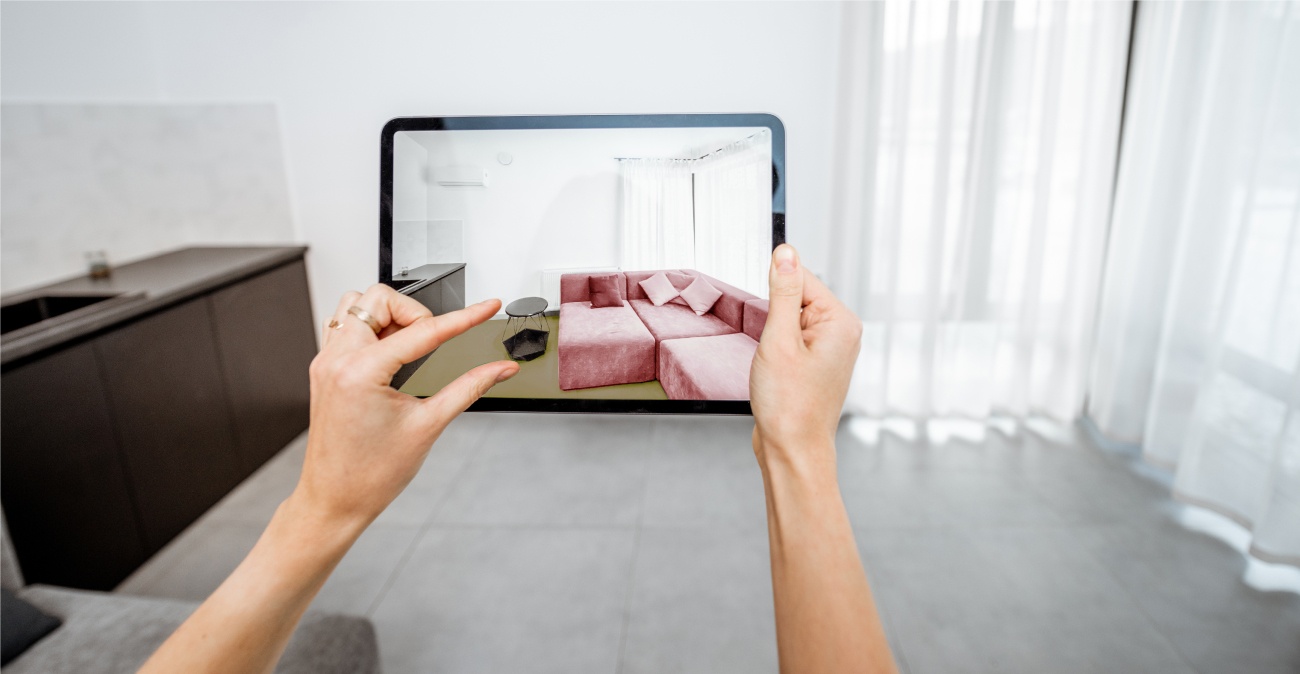 A pair of hands are operating an AR app on an Ipad. A pink sofa and small coffee table are shown on the screen