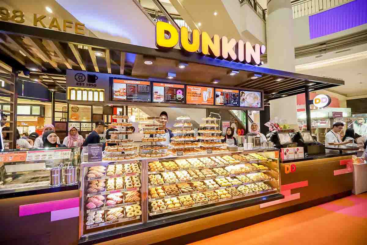 Dunkin’ kiosk in Suria KLCC with a wide variety of Dunkin’ Donuts arranged in its counter where multiple Dunkin’ staff members are smiling at the camera