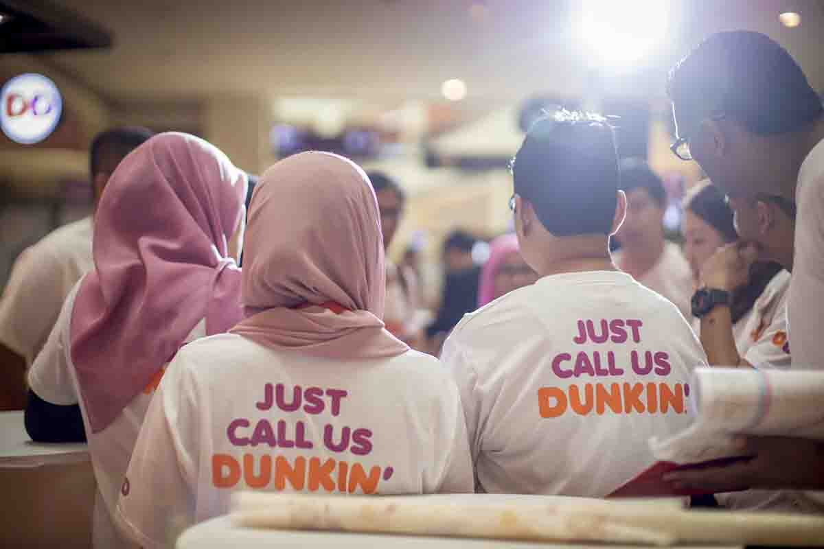 4 staff members of Dunkin’ Donuts wearing t-shirts with ‘Just Call Us Dunkin written on the back of it and their backs are facing the camera
