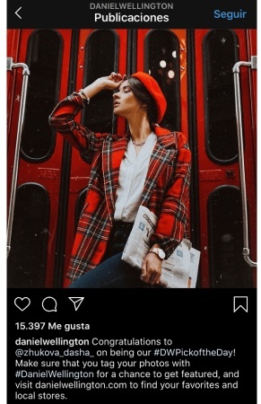 An Instagram post is showing a woman in red jacket and a red hat holding a newspaper. She’s wearing a Daniel Wellington watch on her left hand.