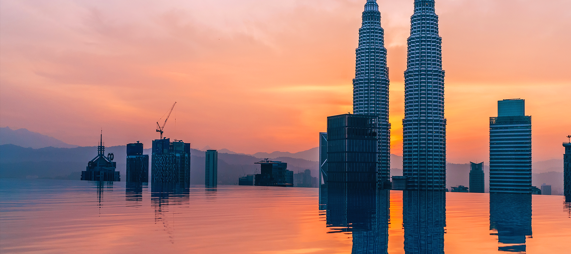 A shot of an infinity pool with the Petronas Twin Towers and other buildings in the background during sunset